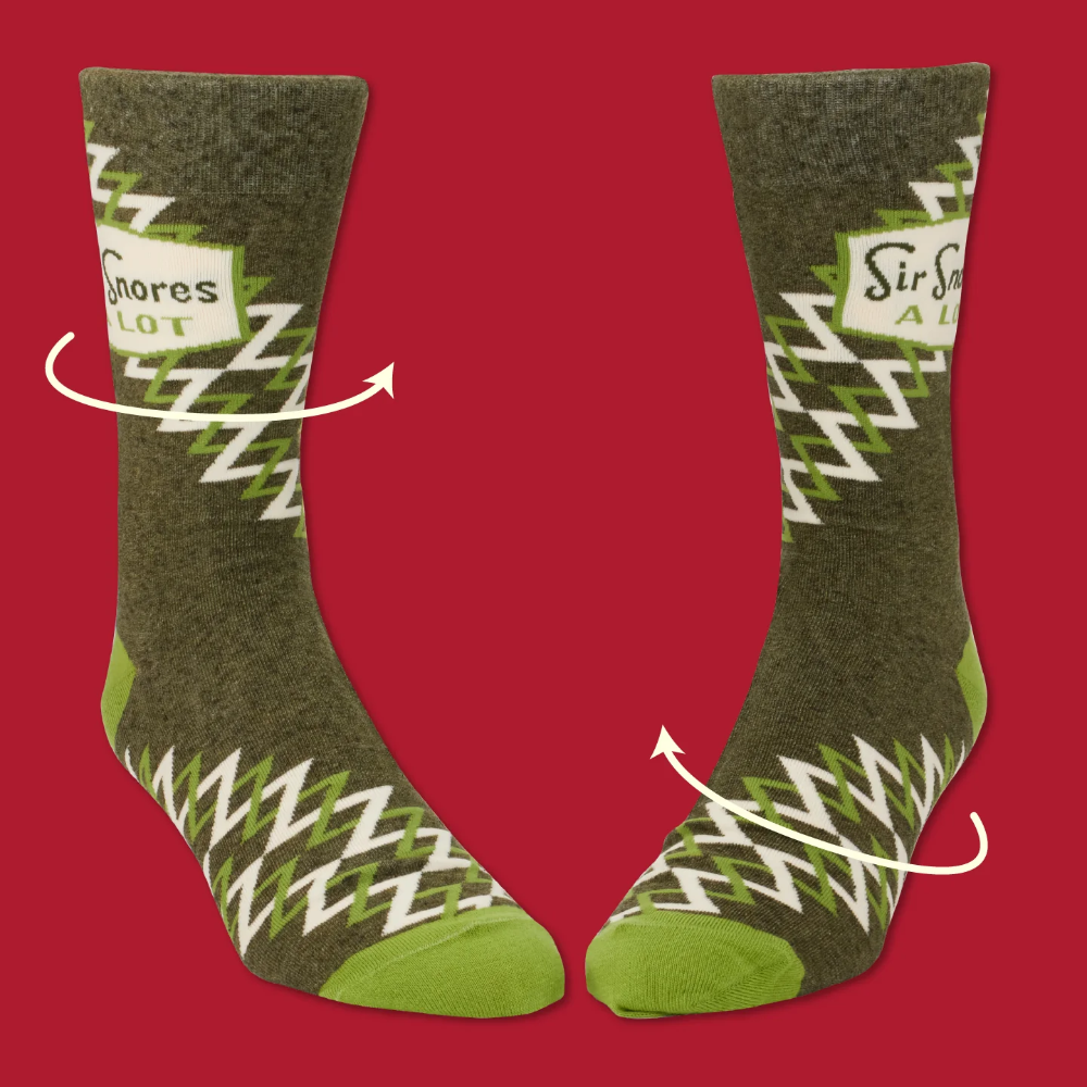 A pair of crew socks shown on a red background with white arrows indicating stretch. The socks are olive green with a white and lime green zigzag pattern and bright green toes and heels.