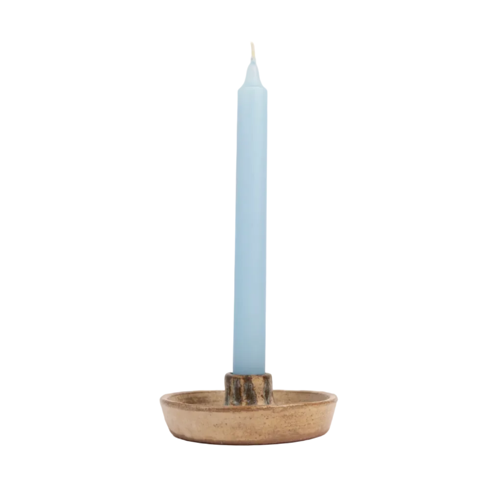 A light blue taper candle standing upright in a rustic, round ceramic holder with a natural beige and brown glaze, set against a plain off-white background.