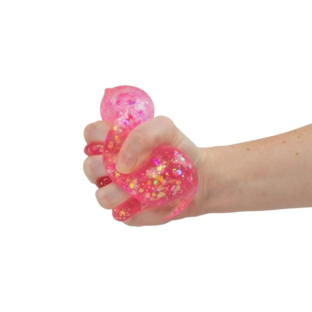 A hand squeezing a translucent pink stress toy filled with glitter, shown against a plain white background.