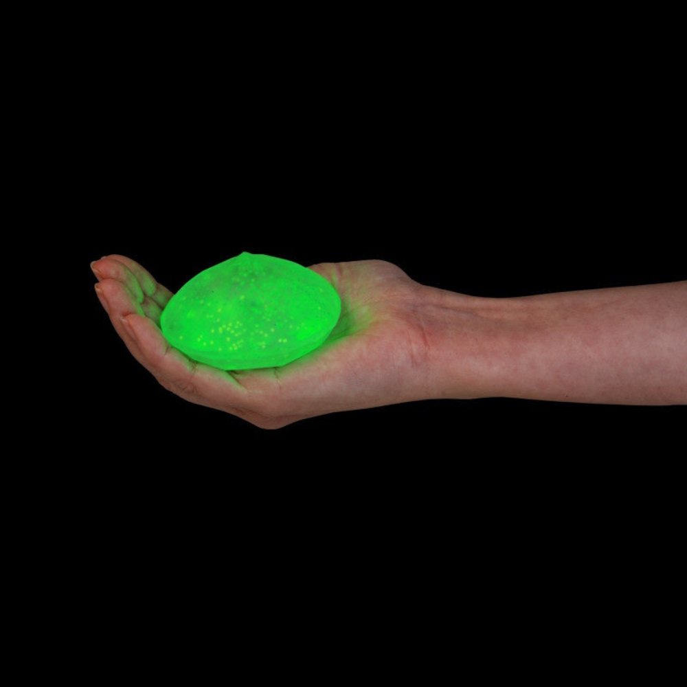 A glowing neon green stress ball being held in a person's open palm against a solid black background.