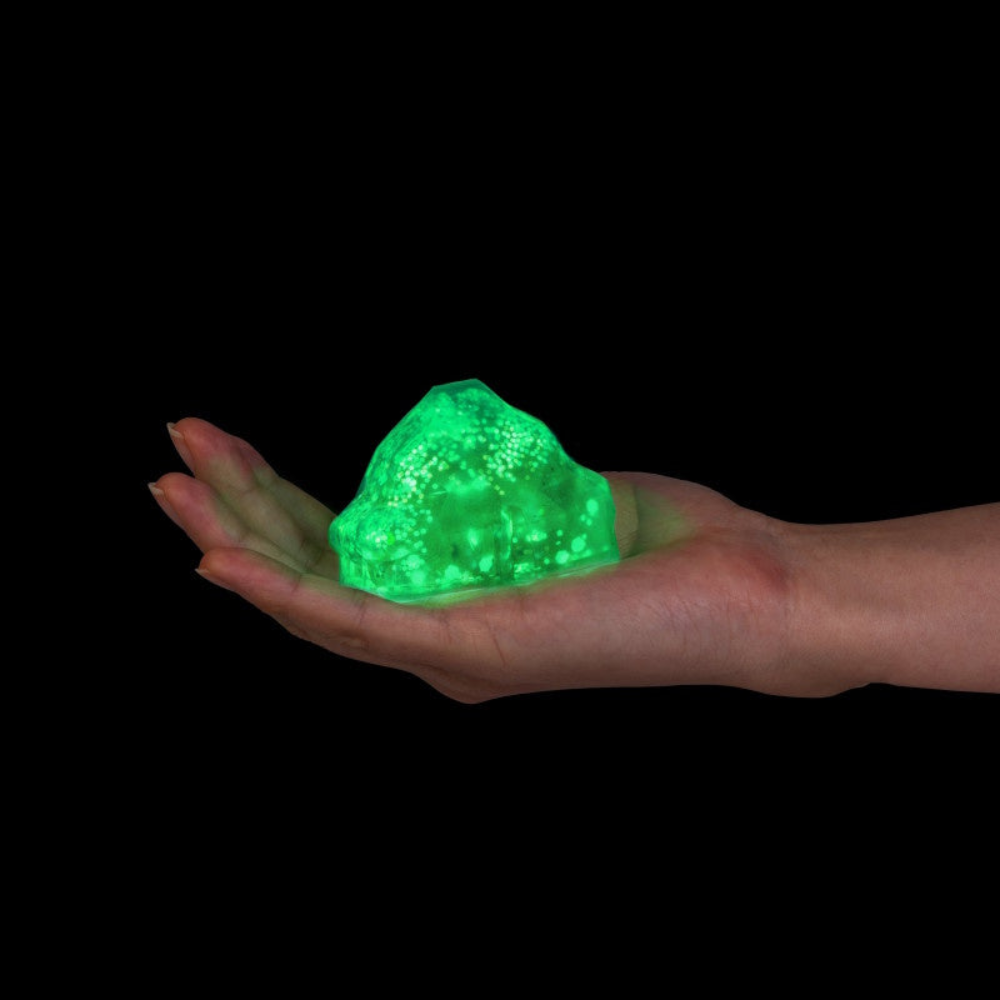 Hand holding a glowing green rock-like object against a black background