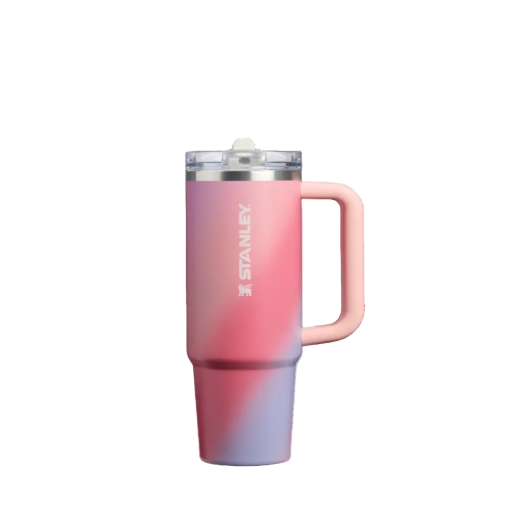 Stanley travel tumbler with a pink and purple gradient finish, featuring a light pink handle, a clear lid with a white straw, and the Stanley logo printed vertically on the side.