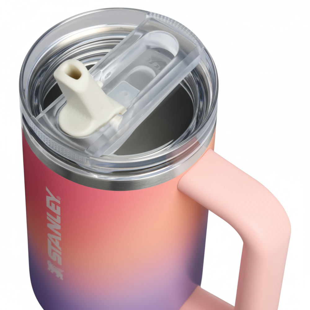 Close-up of a Stanley insulated tumbler with a pink body, clear lid, and light pink handle. The Stanley logo is visible on the lower left side of the tumbler.