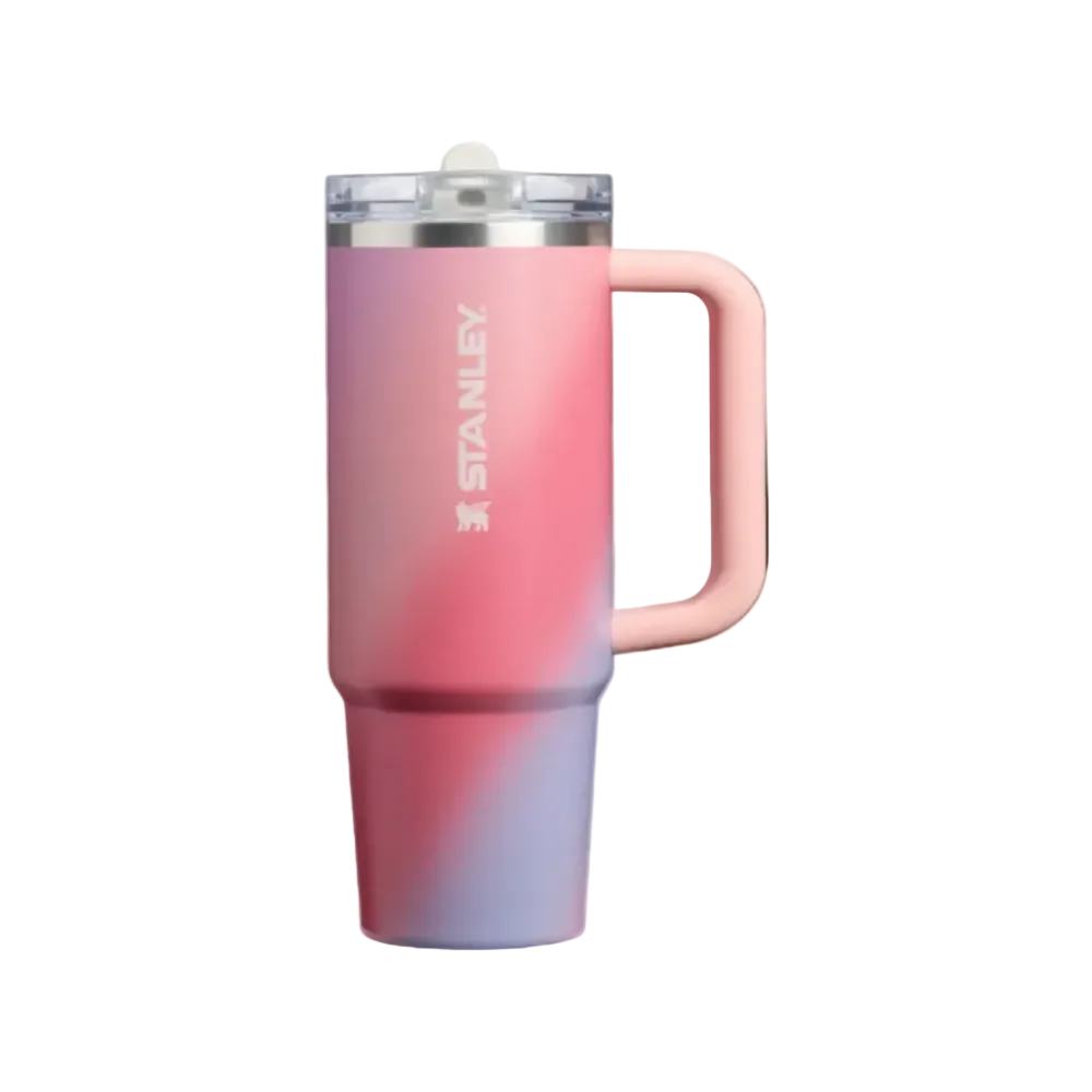 Stanley travel tumbler with a pink and purple gradient finish, featuring a light pink handle, a clear lid with a white straw, and the Stanley logo printed vertically on the side.