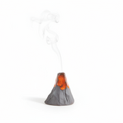 A miniature gray volcano figurine with glowing orange lava and white smoke rising from its top, set against a dark gray background.