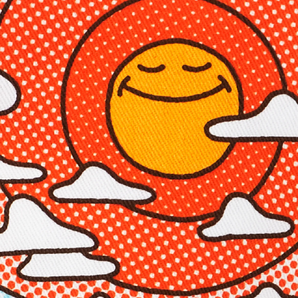 A close-up of a patterned fabric featuring a stylized sun, clouds, and dotted geometric shapes. A dark blue circular badge with white text reads 'Made from 100% cotton'.
