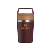 Stanley insulated travel tumbler with a dark burgundy body, a tan lid, and a matching carry loop handle, shown on a plain white background.
