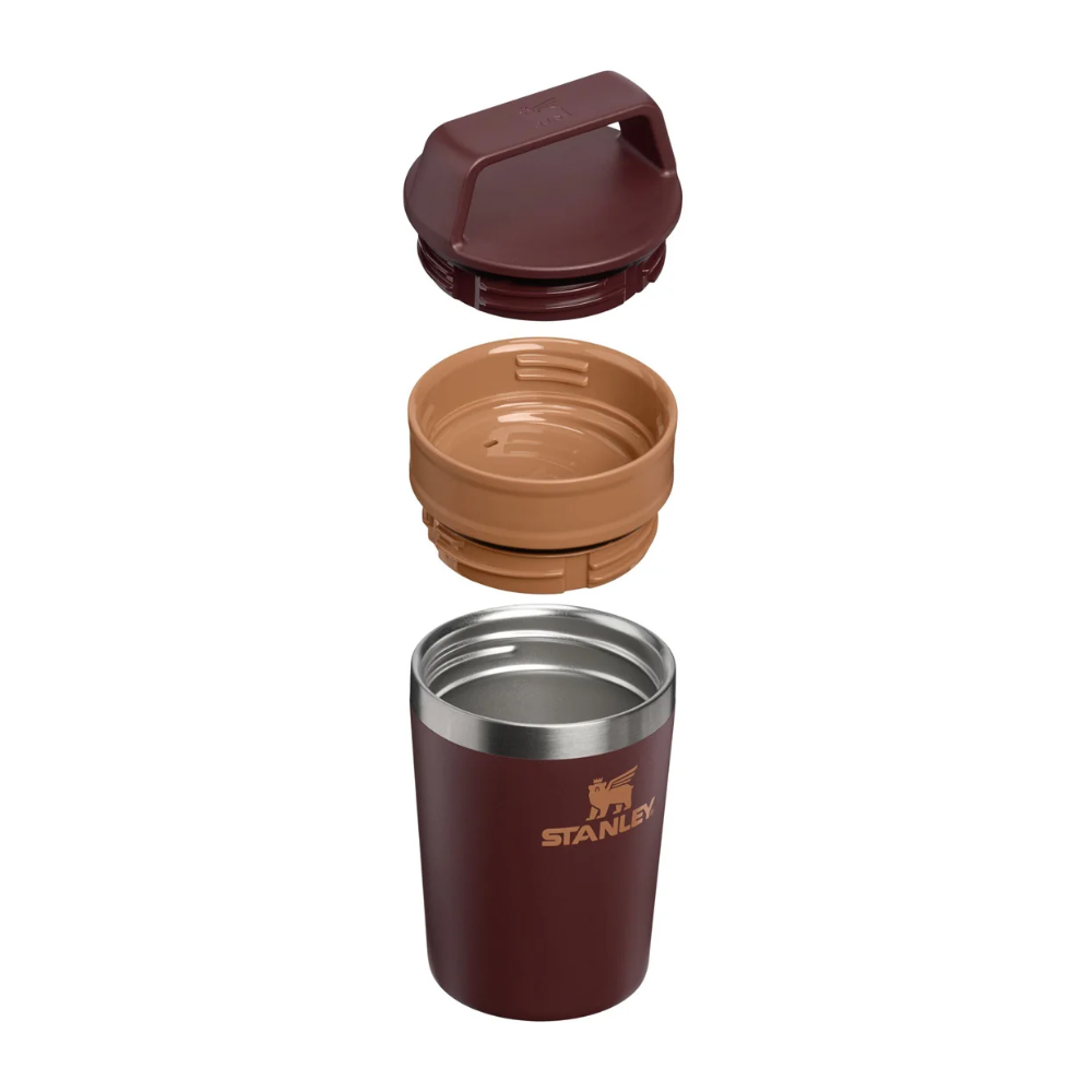 A stainless steel Stanley travel tumbler with its three interchangeable lids shown vertically floating apart against a white background. The tumbler body is dark burgundy with a gold Stanley logo, while the lids are burgundy, tan, and silver.