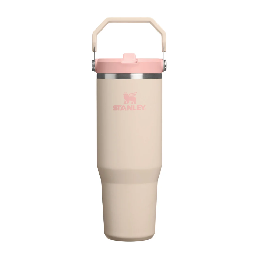 A Stanley insulated travel tumbler in a light beige color with a pink lid and handle, shown against a plain white background.