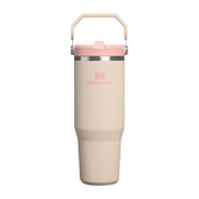 A Stanley insulated travel tumbler in a light beige color with a pink lid and handle, shown against a plain white background.