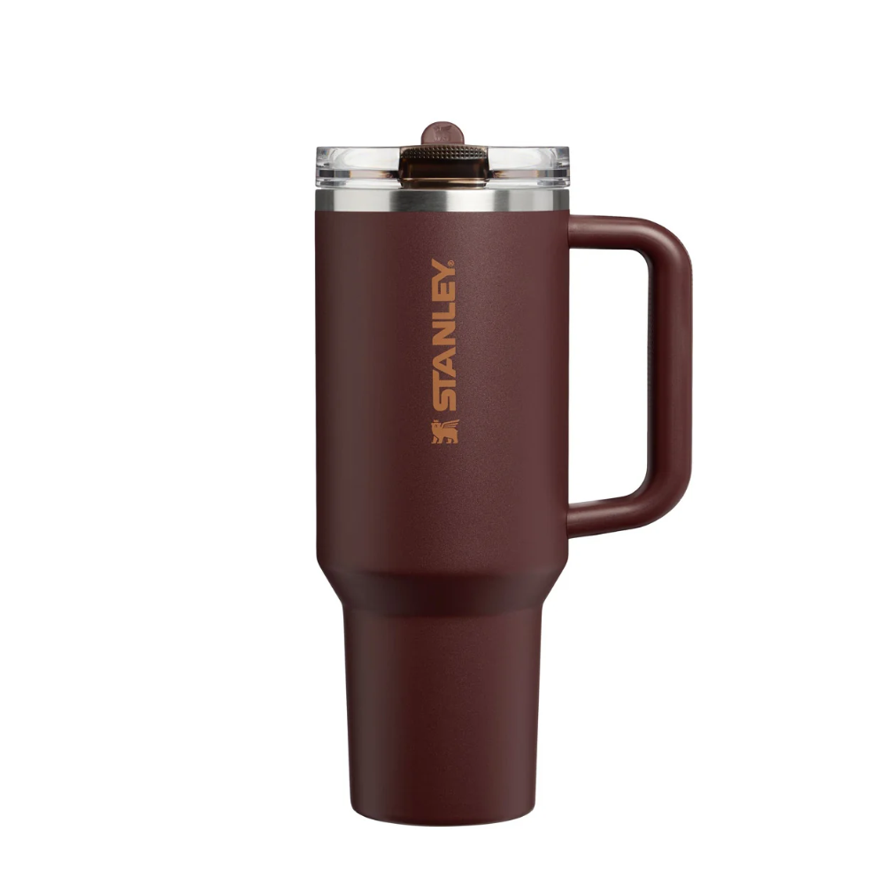 Stanley travel mug in a matte dark reddish-brown color with a gold logo, featuring a clear lid with a brown straw and a side handle, shown on a plain white background.