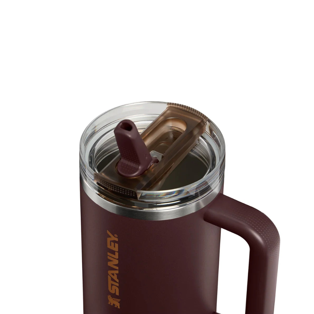 Stanley vacuum-insulated tumbler in dark burgundy with a clear lid, brown flip-top straw, and side handle, shown on a white background.