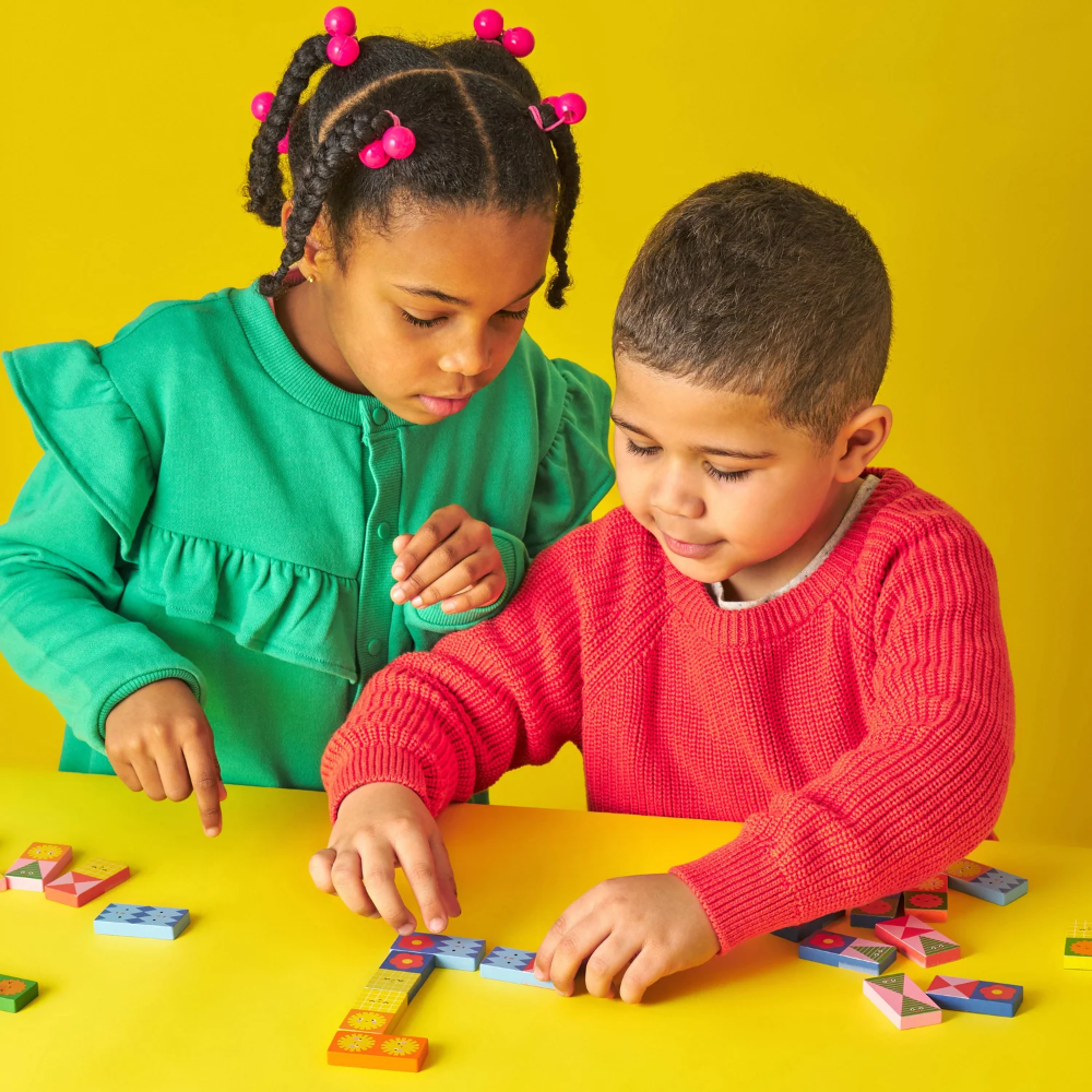 Two children playing with colorful building blocks on a yellow background