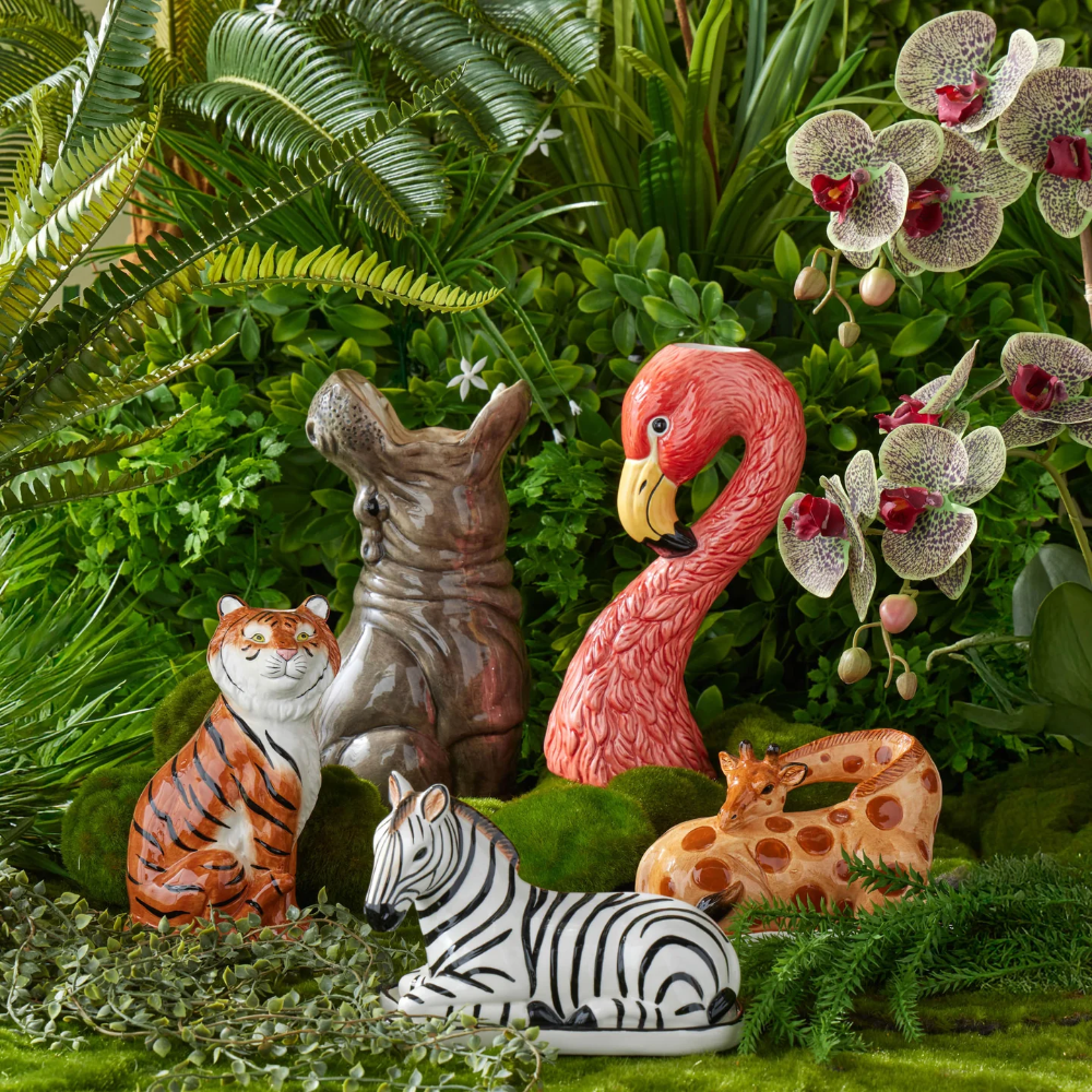 Garden statues of a tiger, zebra, flamingo, and snake among greenery and flowers.