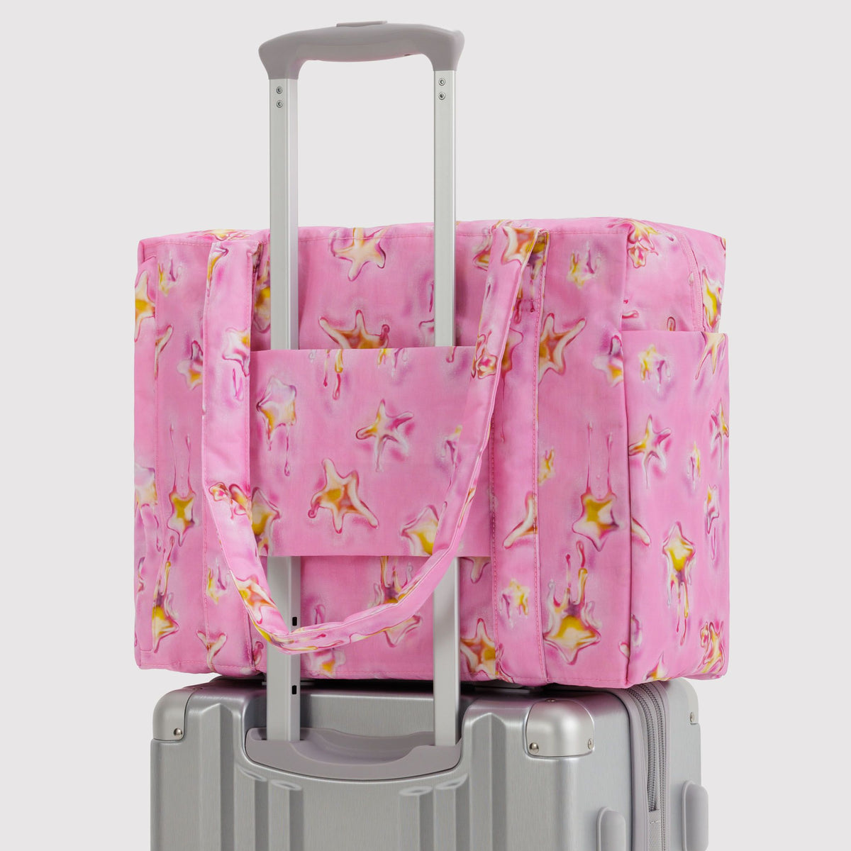 Pink floral-patterned tote bag on a gray suitcase against a white background