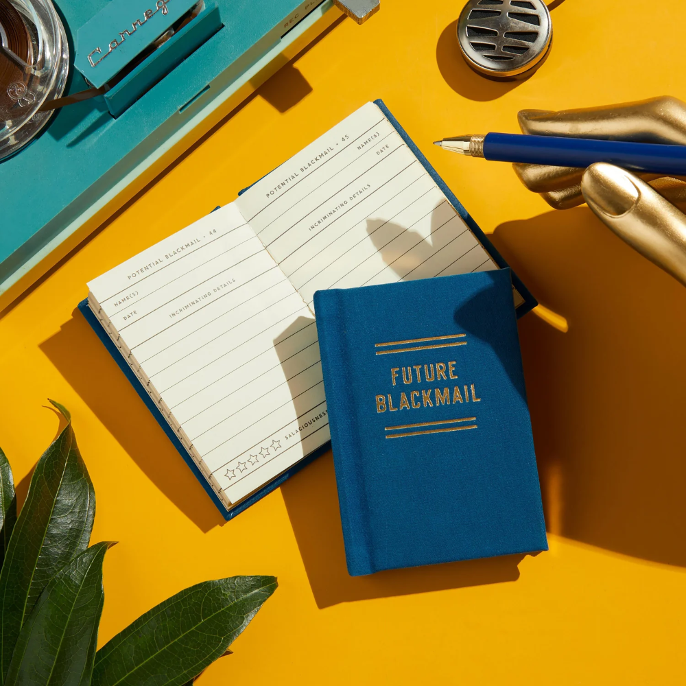 Blue notebook titled 'Future Blackmail' on a yellow surface with a pen and vintage typewriter.