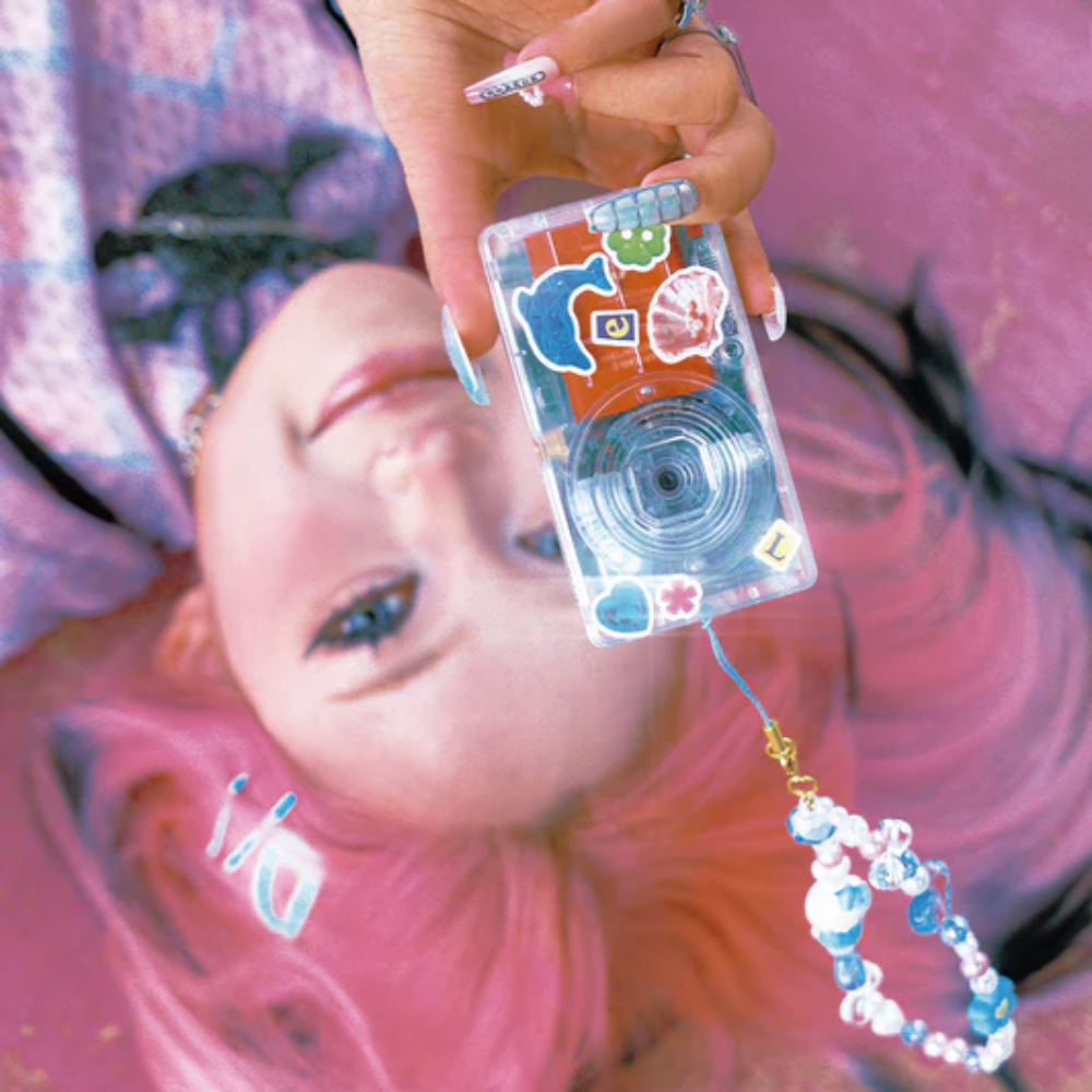Person holding a clear cassette tape with colorful designs, wearing a pink headscarf.