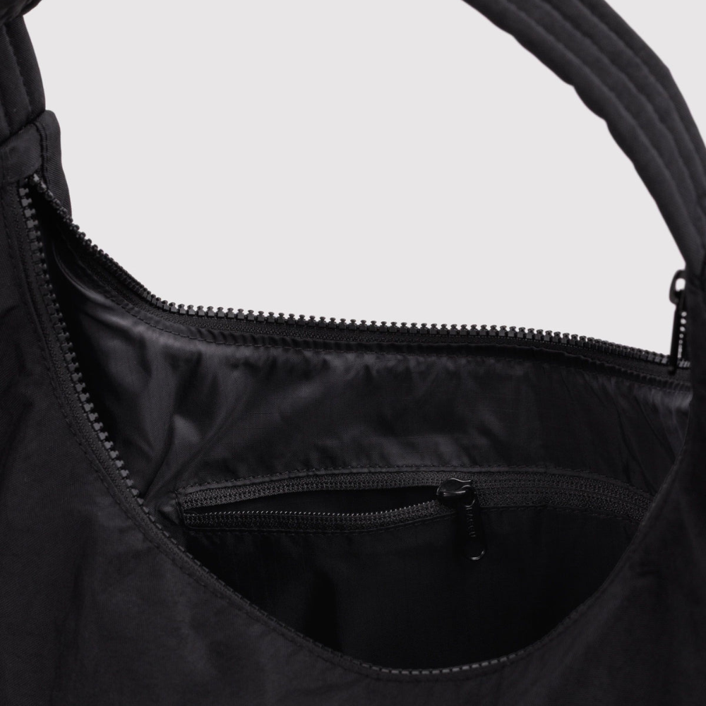 Close-up of a black hobo-style shoulder bag showing the interior with a top zipper and a smaller zippered pocket, set against a light gray background.