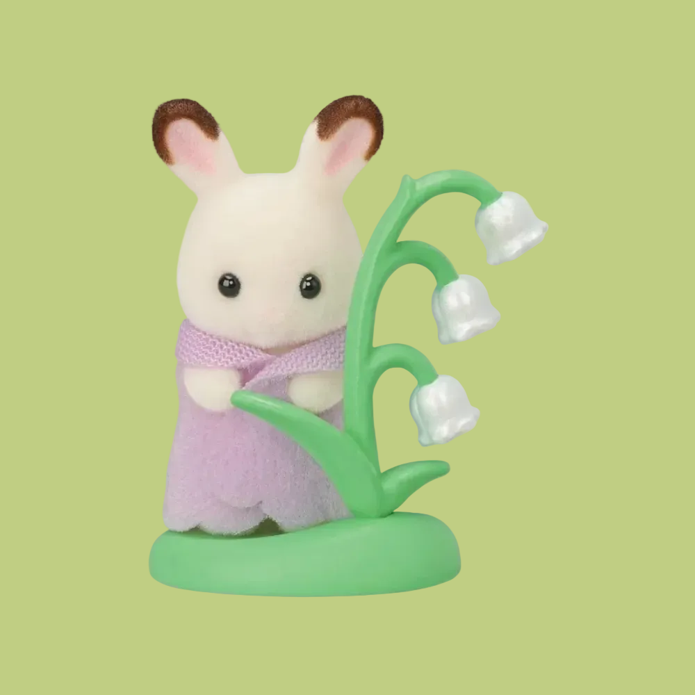 A Sylvanian Family-style rabbit figurine with cream fur, brown-tipped ears, and a pink bow, standing beside a green lily-of-the-valley style plant with three white bell-shaped flowers on a plain white background.