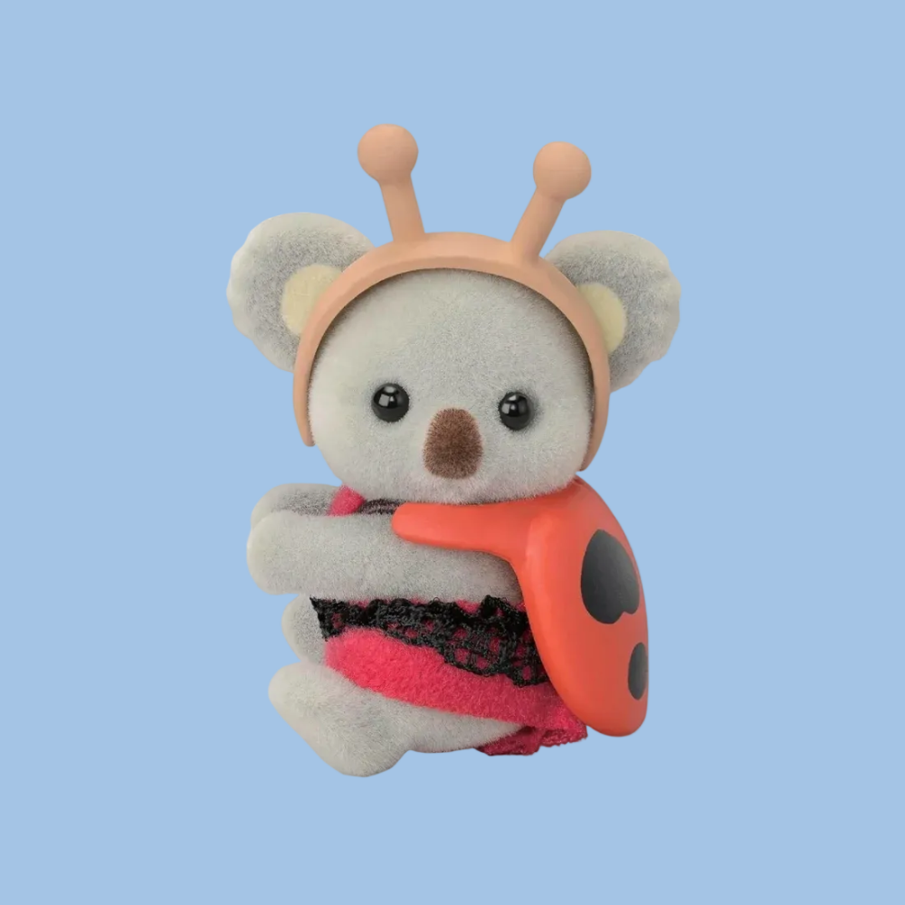 A small plush koala toy wearing a peach antler headband and a red-and-black ladybug outfit, posed against a plain white background.