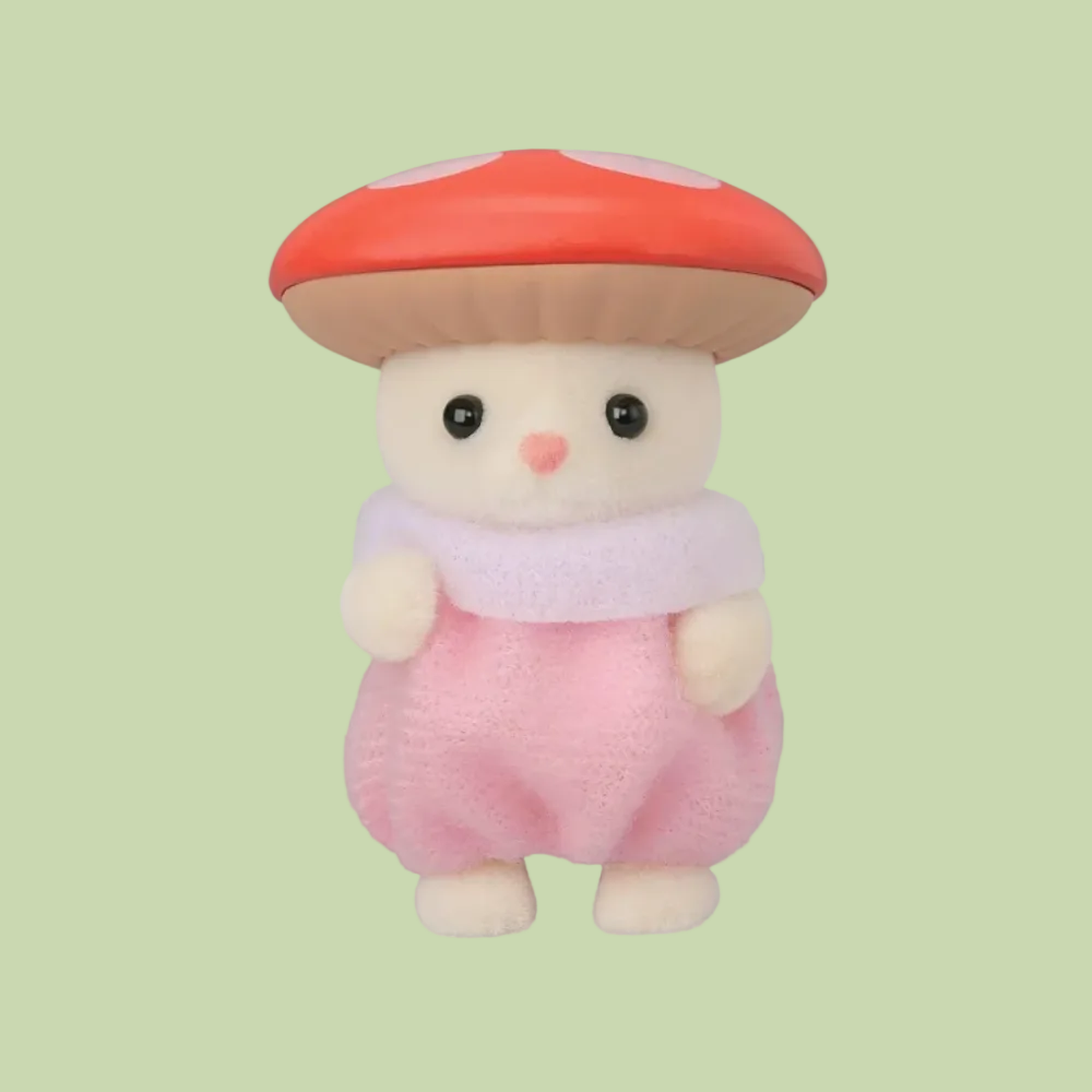 A small plush toy character shaped like a mushroom with a cream-colored face and hands, wearing a red-orange cap with white spots, a pale pink scarf, and a pink body, shown on a plain white background.