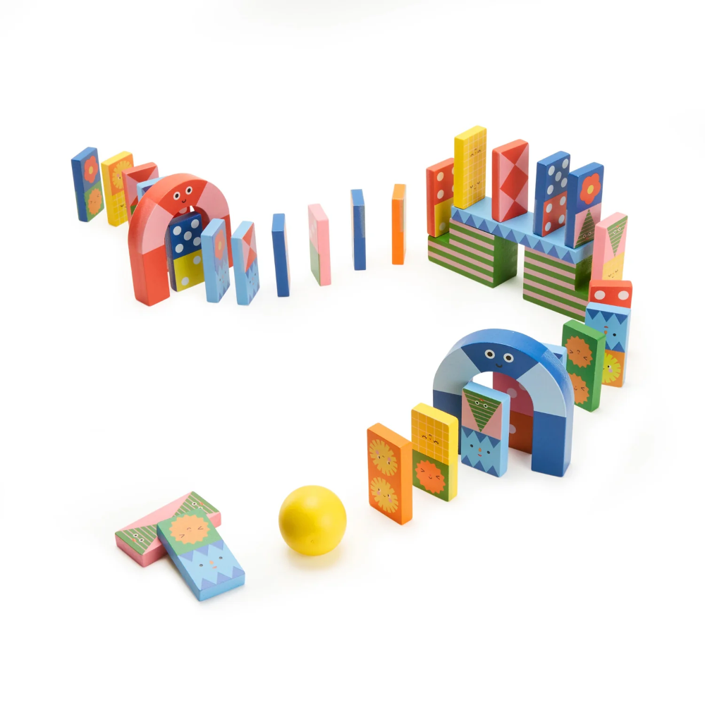 A colorful wooden domino block set arranged in a playful layout on a white background, featuring geometric arches, patterned dominoes, and a yellow ball.