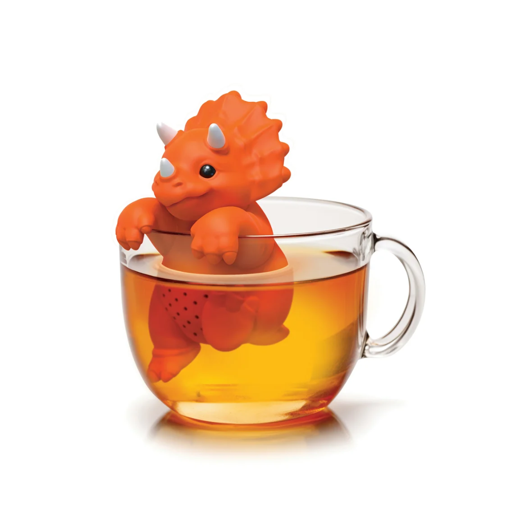 Orange dinosaur-shaped tea infuser in a glass of tea on a white background