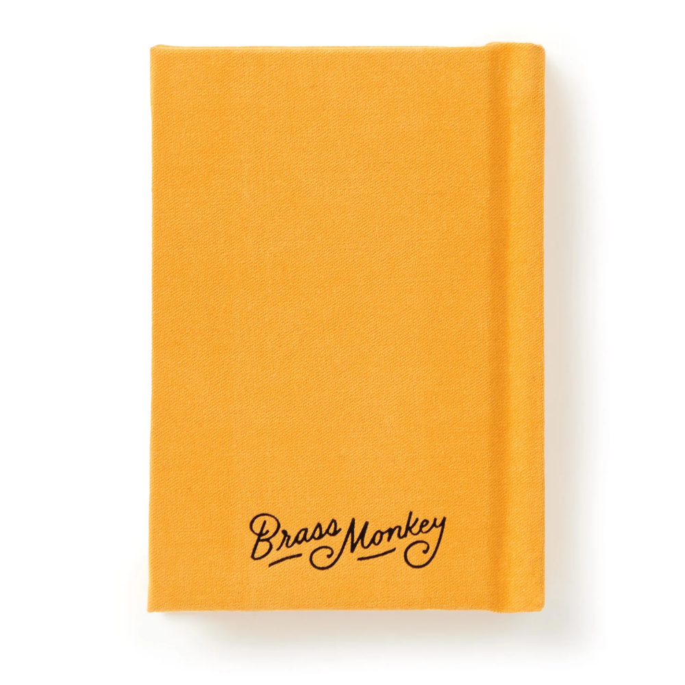 A bright yellow linen notebook with 'Brass Monkey' written in black cursive script near the bottom, shown on a clean white background.