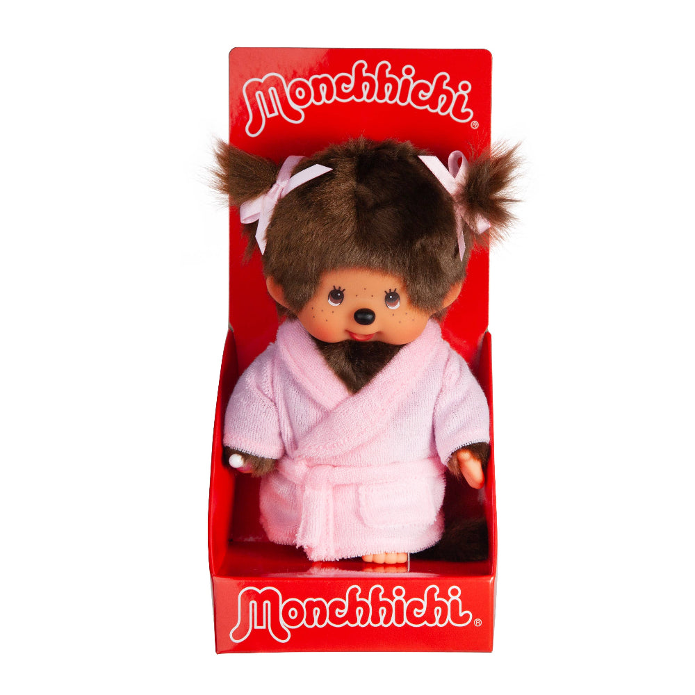 A Monchhichi plush toy doll in its original red window box packaging, featuring brown hair in pigtails with white bows and a pink plush robe.