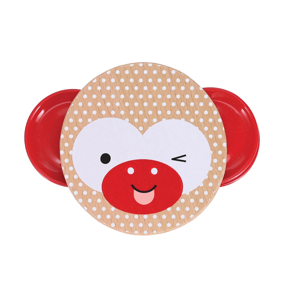 A round wooden plate with a smiling monkey face tambourine, featuring a beige wood-grain background with white polka dots, a white heart-shaped face, and a red snout. Red plastic side supports are visible behind it on a plain white background.