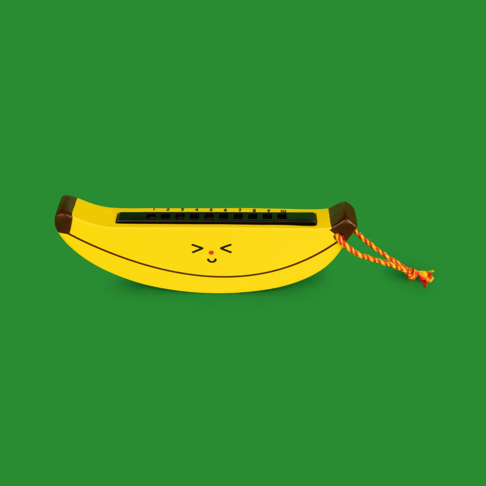A novelty banana-shaped toy or instrument in bright yellow with a small cartoon face and a braided orange-and-red hanging cord, shown on a solid green background.