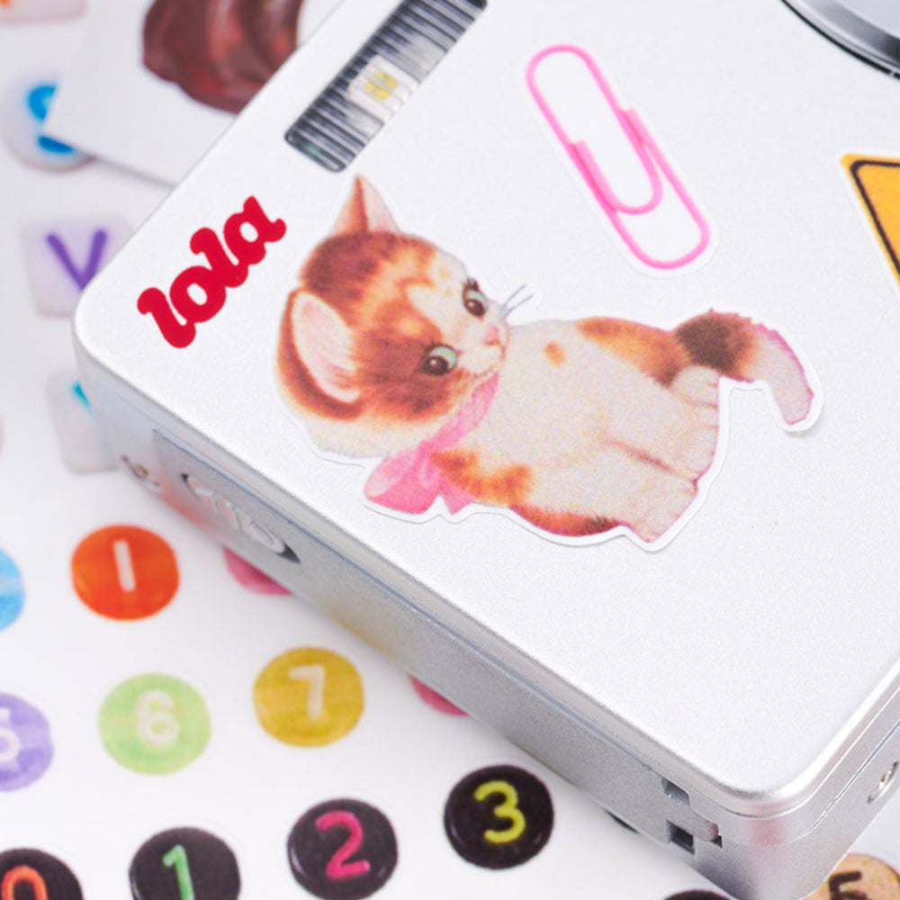 Small electronic device with a cat sticker labeled 'lola' on a colorful background with numbers and letters.