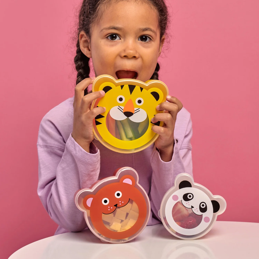 Child holding a tiger-shaped plate with two other animal-themed plates on a pink background