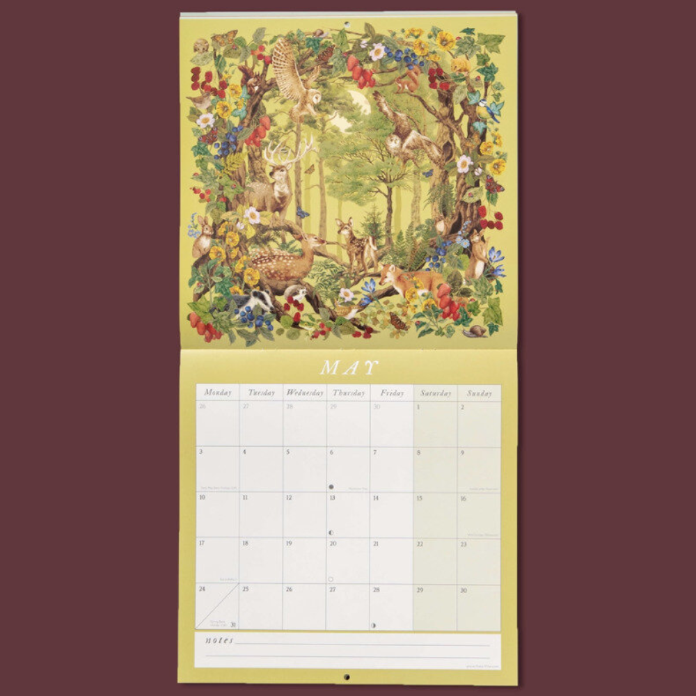 Vintage-style hanging calendar page for May, showing a large illustrated forest and deer scene on the upper section and a monthly calendar grid labeled MAT on the lower section, against a solid dark burgundy background.