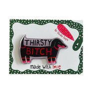 A novelty enamel pin shaped like a dachshund with the text 'THIRSTY BITCH' in red and white, displayed on its green and white backing card which reads 'made with love' and features a pink 'Machee by Studio Soph' logo.