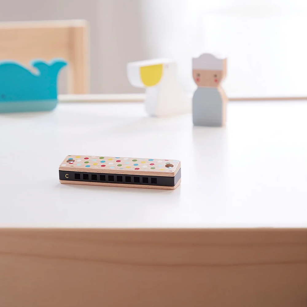 Small wooden harmonica on a white surface with toys in the background