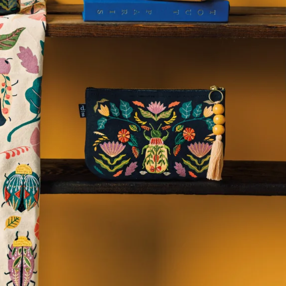 Decorative items including a mug, pouch, and towel with beetle designs on a wooden shelf against an orange wall.
